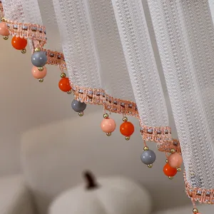 Dettaglio di tenda in pizzo bianco con perline colorate, elegante decorazione.
