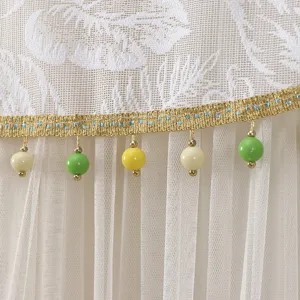 Close-up detail of white mesh curtain with gold trim and colorful hanging beads texture.