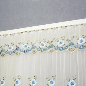 Vue détaillée du rideau en tulle blanc avec broderie florale bleue et bordure en dentelle.