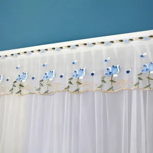 Détail de rideau transparent blanc avec broderie florale bleue et bordure dorée élégante.