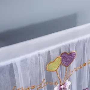 Dettaglio copri TV in pizzo bianco con ricamo a cuore e delicata trama di tessuto mesh.