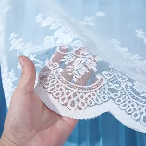 Close-up detail of light blue lace curtain fabric with delicate white floral embroidery.