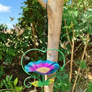 Metal heart bird feeder hanging from tree branch in lush garden with hummingbirds