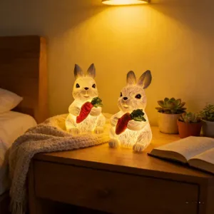 Deux figurines de lapins en résine lumineuses avec carottes sur une table de nuit