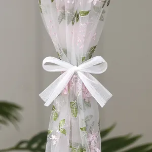 Detailed view of white sheer door curtain with delicate pink floral embroidery and elegant bow.