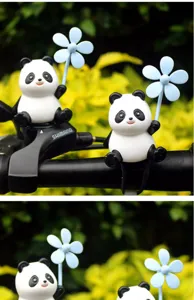Close-up detail of cute panda figurine holding a blue windmill prop mounted on bike handlebar.