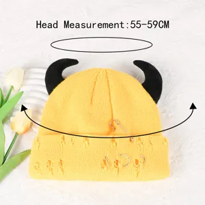 Close up detail of yellow knit beanie with devil horns, metal pin and ring decor.