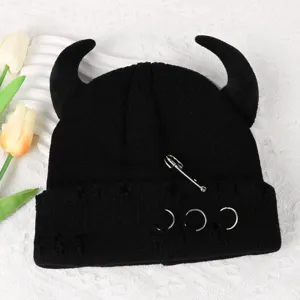 Black knitted beanie with devil horns, metal safety pin, and ring decor. Detail view.