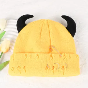 Yellow knitted beanie detail showing black devil horns, safety pin, and ring piercing decors.