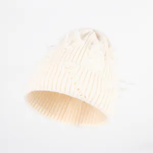 Detailopname van de versleten gebreide muts in off-white met unieke gescheurde textuur.