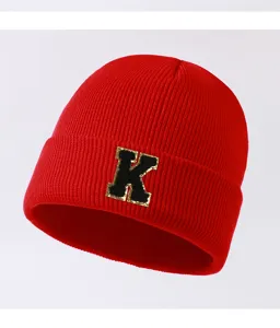 Close-up of red knit beanie hat featuring a bold black and gold letter K patch detail.