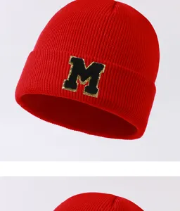 Close-up detail of red winter knit beanie with black gold trimmed letter M patch, warm hat.