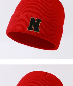Red knit beanie hat detail view featuring a stylish black and gold letter N patch design.