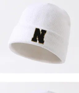 Nahaufnahme einer weißen Winter-Beanie-Strickmütze mit schwarzer Buchstabenstickerei, gemütlich.
