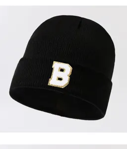 Detailed view of black knitted beanie hat with a stylish white letter B patch on front.