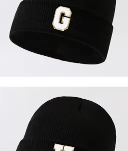 Detail view of black knit beanie hat featuring white letter patch, winter warm headwear