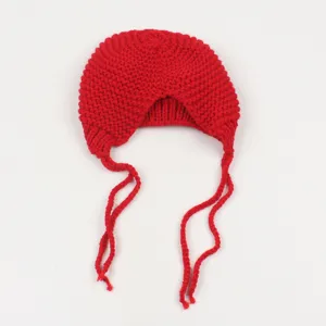 Detalle en primer plano del gorro de punto rojo con orejeras cómodas y largos cordones trenzados.