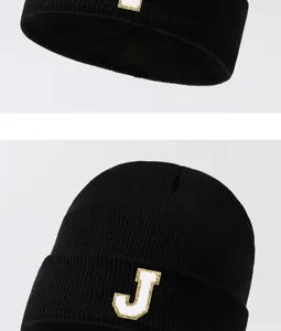 Black knit beanie hat detail view with white and gold letter J patch, stylish streetwear.