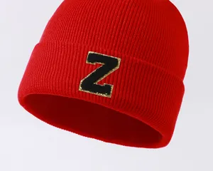 Close-up of a red knitted beanie hat featuring a black and gold glitter letter Z patch.