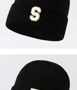 Detailed view of black knitted beanie hat with white and gold letter S patch decoration.