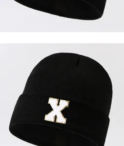 Close-up detail of black knit beanie hat featuring a stylish white letter X patch.