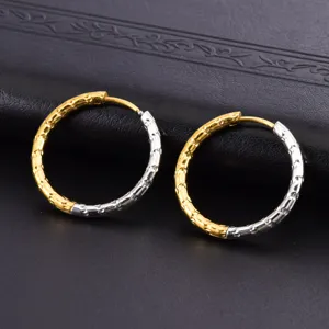 Detail of two-tone gold and silver textured hoop earrings on black leather background.