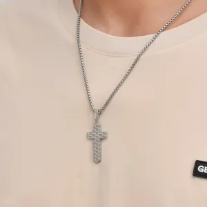 Detail shot of a silver cross pendant necklace worn on a casual beige t-shirt.