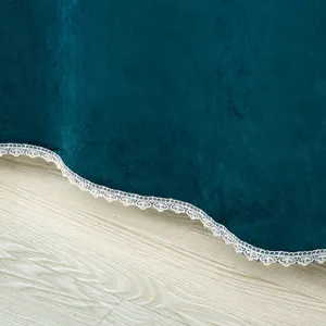 Detailed close-up of dark teal velvet curtain bottom hem featuring delicate white lace trim.