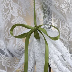 Close-up view of elegant white lace curtain with olive green ribbon bow, vintage home decor detail.