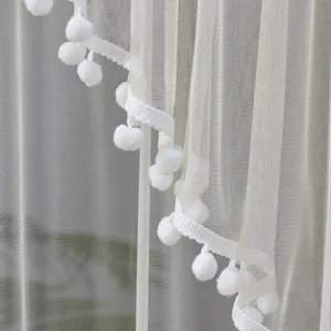 White sheer curtain detail showing delicate mesh fabric and cute white pom-pom lace trim.
