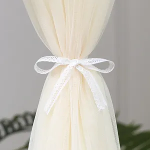 Close-up detail of beige sheer window curtain featuring a delicate white lace bow tie-back.