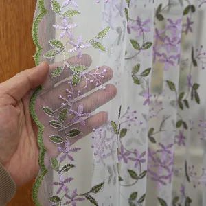 White sheer curtain detail showcasing delicate purple floral embroidery and green leaf patterns.