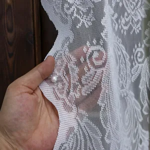 Close-up detail of white lace fabric curtain showing fine mesh texture and vintage pattern.