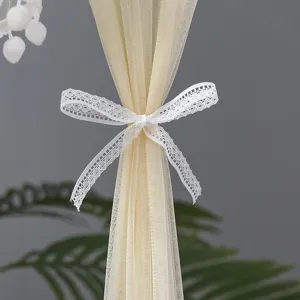 Close-up detail of sheer mesh curtain with elegant white lace bow tie, soft beige fabric.