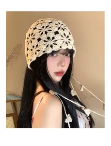 Dettaglio ravvicinato di un cappello beige all'uncinetto con fiori e nappine pendenti.