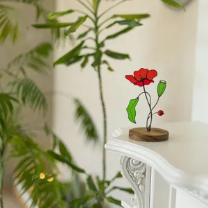 Handcrafted stained glass poppy flower ornament on a wooden base in a sunlit room