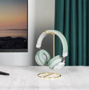Minimalist gold metal headphone stand shown in a home office setting holding headset
