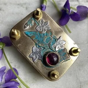 Makroansicht einer Mini-Blumenpresse aus Metall mit Gravuren und einem lila Edelstein-Besatz