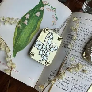 Nahaufnahme einer Mini-Blumenpresse aus Metall mit Maiglöckchendesign auf antikem Buch
