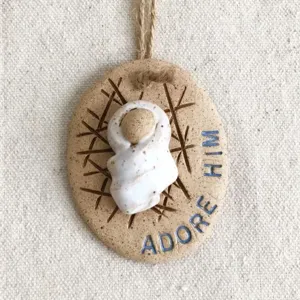 Close-up of rustic Baby Jesus ornament featuring engraved Adore Him text and hemp rope
