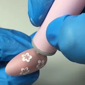 Nahaufnahme eines Nagelkunst-Stempelstifts, der Blumenmuster auf einen Nagel aufträgt.
