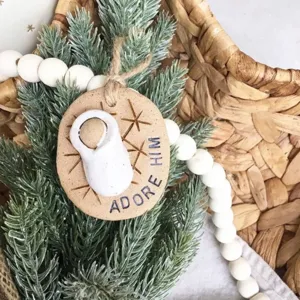 Close-up detail of a rustic Baby Jesus ornament with Adore Him text on pine branches