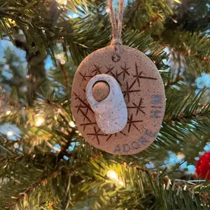 Detailed macro view of Baby Jesus Christmas ornament with 'Adore Him' text hanging on a tree