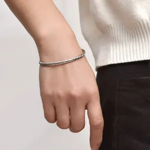 Nahaufnahme eines silbernen, gedrehten Edelstahl-Armreifs am männlichen Handgelenk