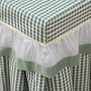 Green gingham table cover with delicate lace and cute yellow daisy embroidery detail for home.
