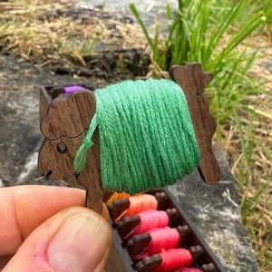 Detail eines schafsförmigen Holzspulenkörpers mit grünem Stickgarn fest umwickelt