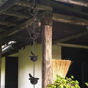 Detailed view of a decorative bronze bird rain chain hanging from a rustic wooden porch structure.