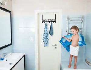 Black iron over the door towel rack with BATH TOWELS text shown in a modern bathroom
