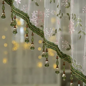 Close-up of vintage lace curtain detail, featuring elegant green beaded fringe and floral embroidery.
