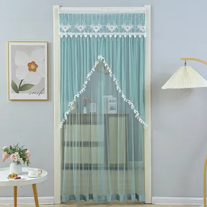 Detail view of a teal mesh door curtain with lace embroidery and decorative pom-pom tassels.